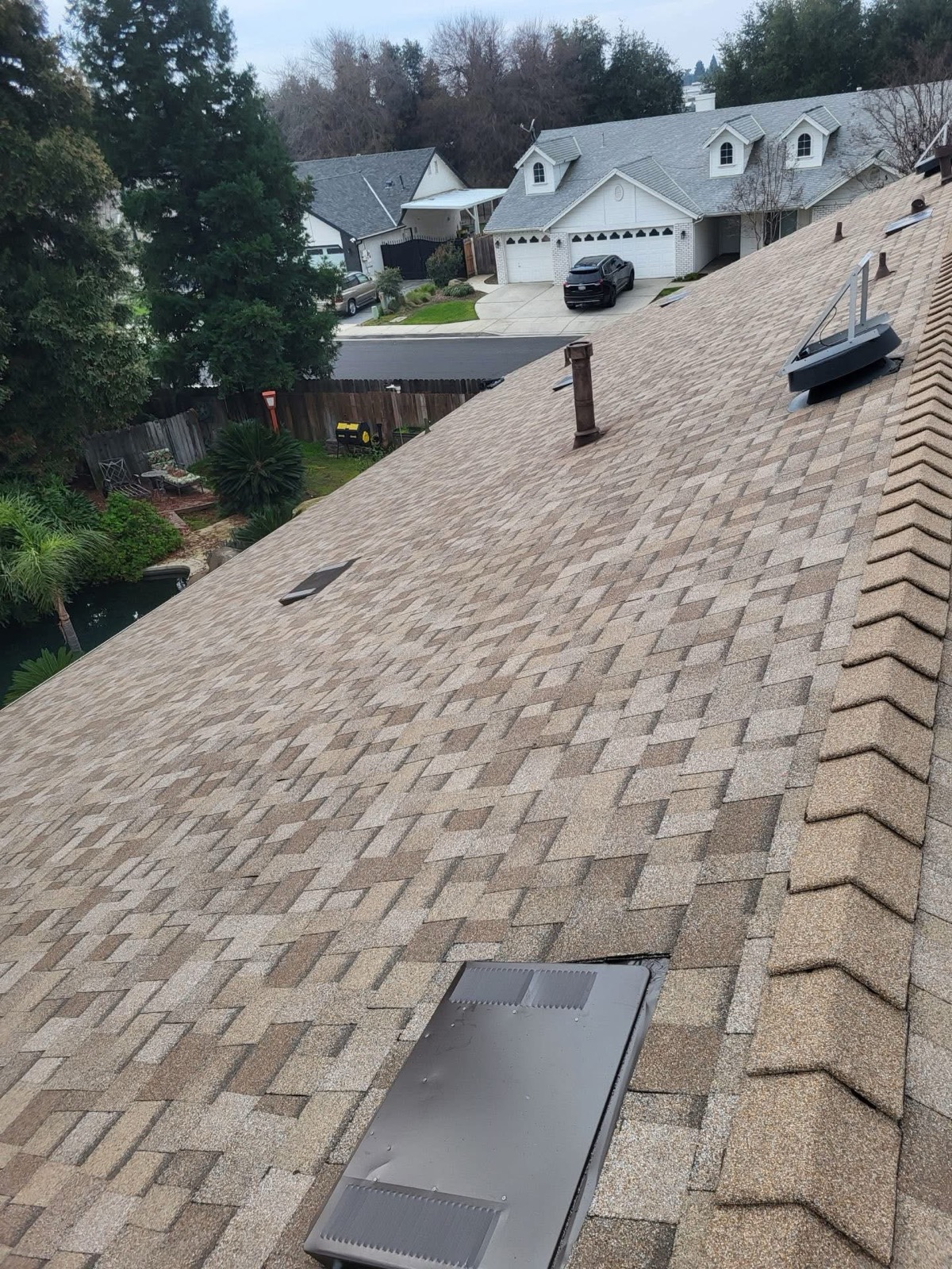 Completed tan architectural-shingle roof with ridge caps and roof vents